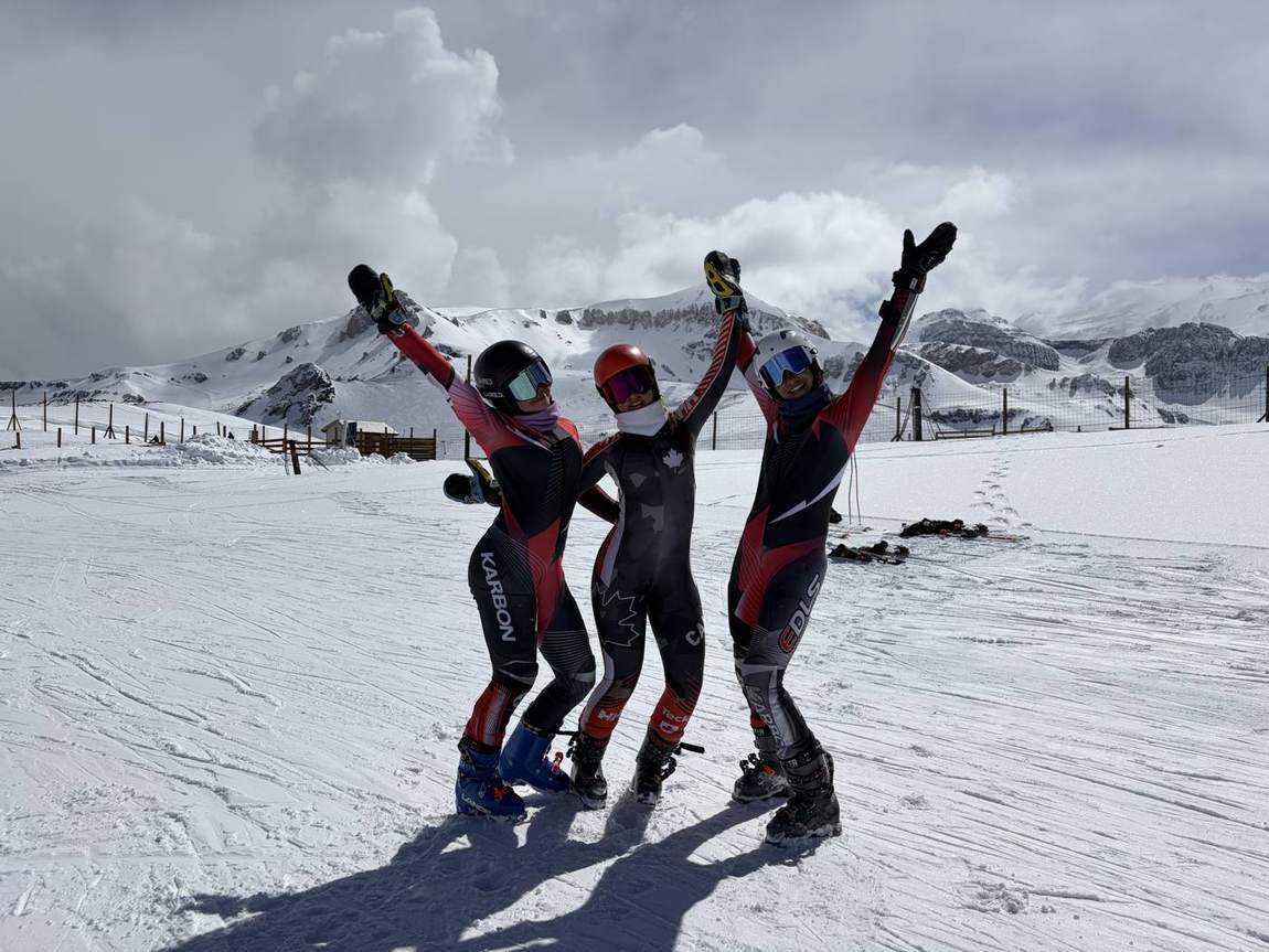 Trois skieuses en combinaison qui lèvent les bras dans la neige